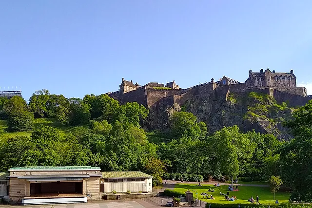 Edinburgh Castle crowning its dark rock above the green slopes of Princes Street Gardens under a clear blue sky