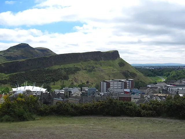 Arthur's Seat and the cliffs of Salisbury Crags rising above the rooftops of Holyrood, with grey clouds above